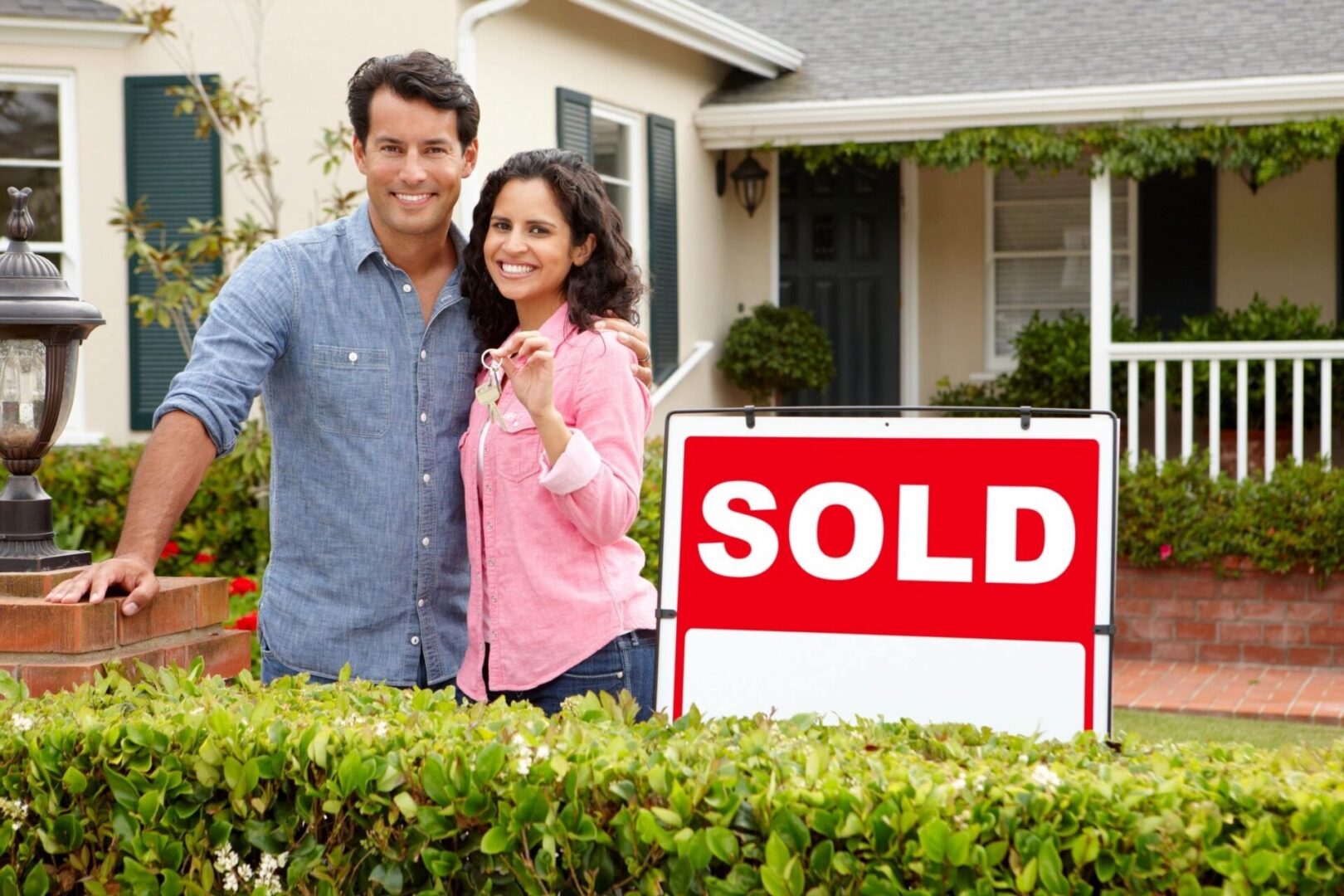 A couple standing in front of their home with the sold sign.